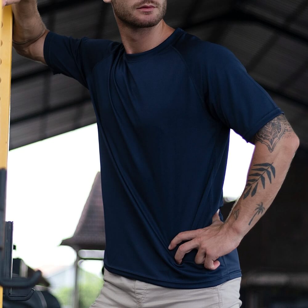 Mann in marineblauem T-Shirt lehnt an einem Fitnessgerät, lässige Haltung.