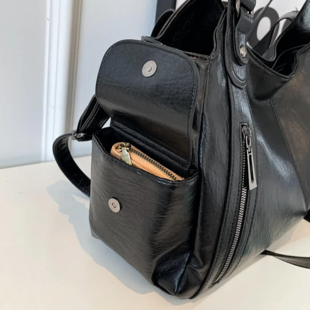 Seitentasche einer schwarzen Handtasche mit Magnetverschluss, in der ein kleines Portemonnaie aufbewahrt wird.