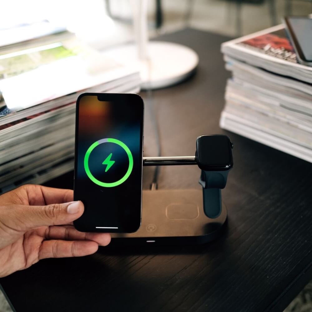Hand hält iPhone über ein MagSafe 3-in-1 Ladegerät – kabelloses Laden für iPhone, Apple Watch und AirPods.