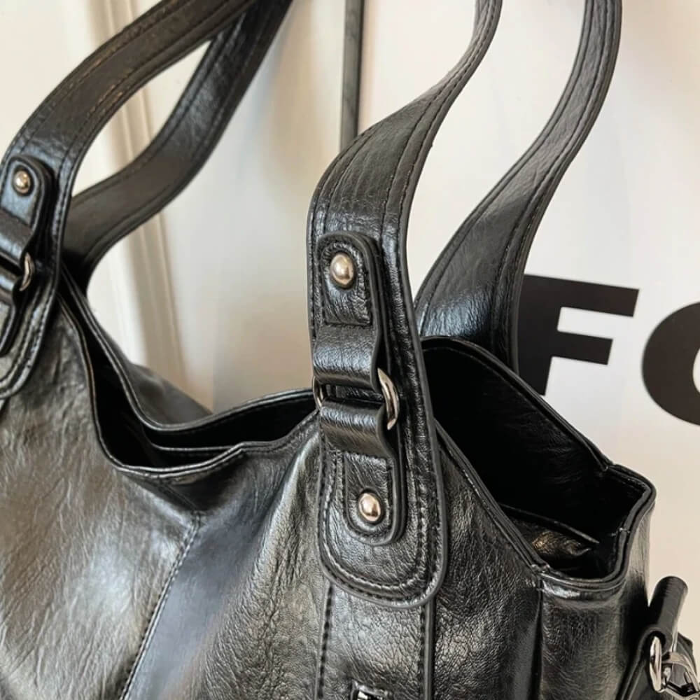 Nahaufnahme einer schwarzen Lederhandtasche mit doppeltem Griff und silbernen Details, vor einem „Focus“-Poster.