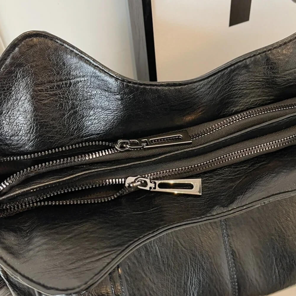 Nahaufnahme einer schwarzen Lederhandtasche mit zwei Reißverschlüssen an der Oberseite für sichere Aufbewahrung.
