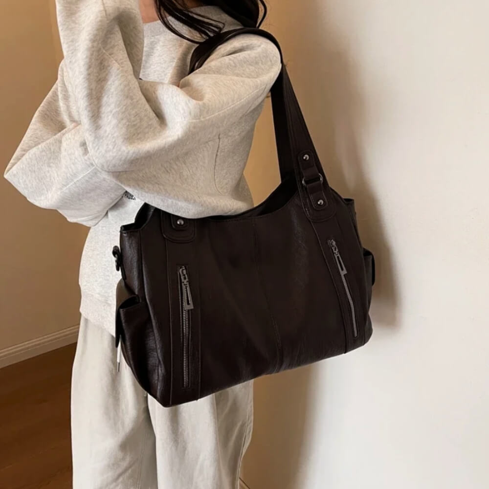 Frau in hellem Outfit trägt eine Espressobraune Lederhandtasche locker über der Schulter.