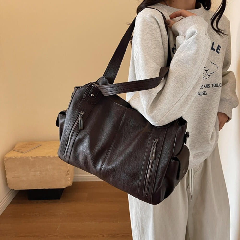 Frau in grauem Sweatshirt trägt eine Espressobraune Lederhandtasche mit mehreren Fächern und Schulterriemen.