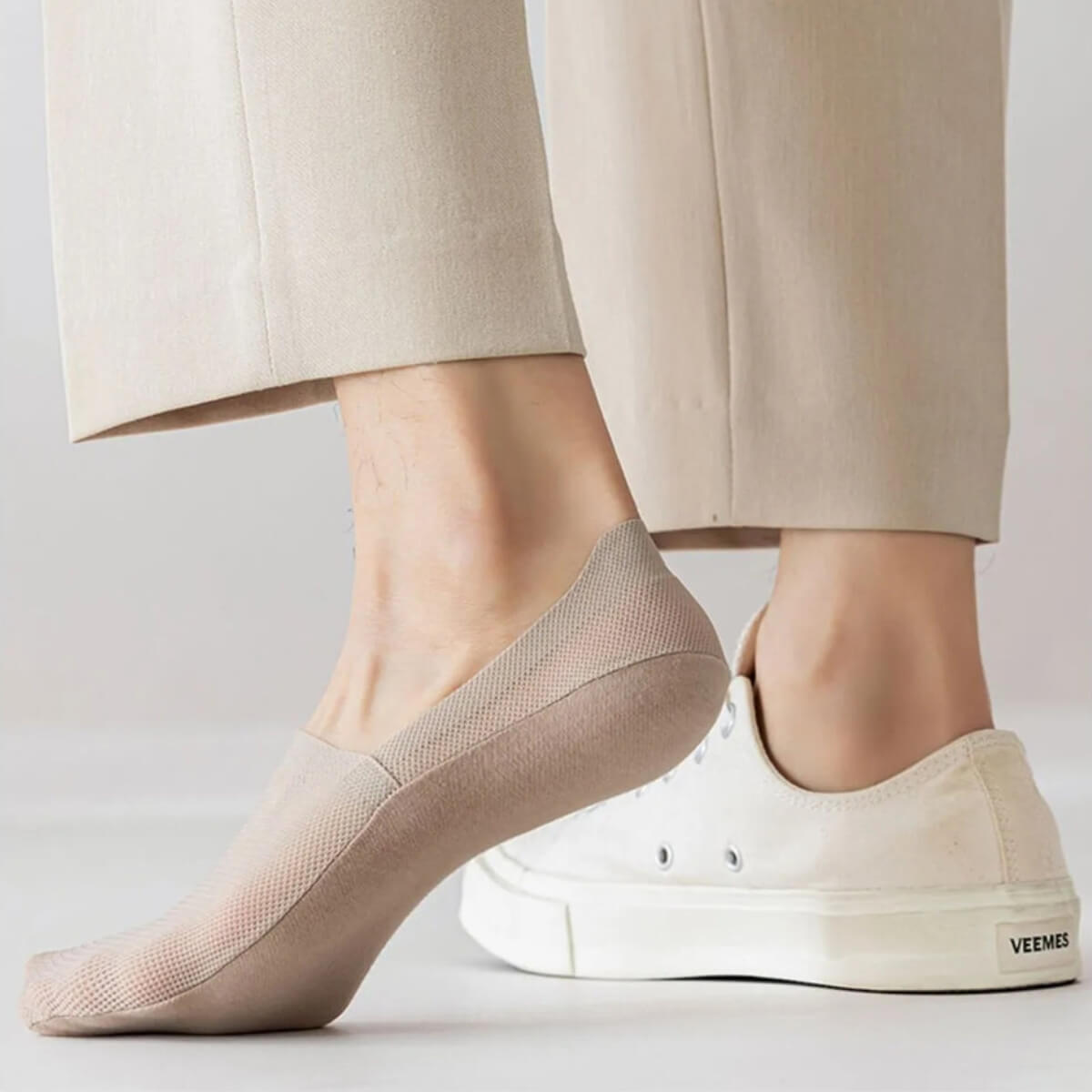 Beige Socke an Füßen, getragen mit hellen Hosen und weißen Sneakers.